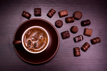 a cup of coffee and chocolate candies on a dark background.