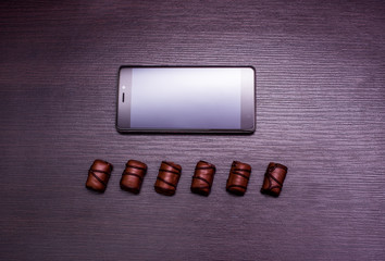 a cup of coffee, chocolate candy and a phone on a dark background.