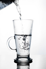 Hand pours water into a glass glass Cup of glass teapot. Shut. Isolated on white background