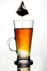 Brewing of hot beverage with tea bag in glass cup on white background