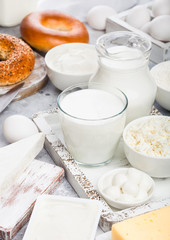 Fresh dairy products in vintage wooden box on white table background. Jar and glass of milk, bowl of sour cream and cheese and eggs. Fresh baked bagel on round chopping board with knife.
