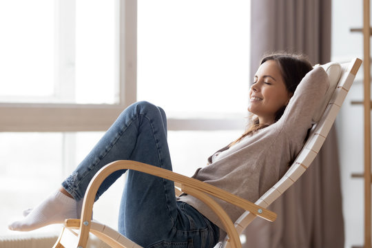 Relaxed calm young woman lounging sitting in comfortable wooden rocking chair breathing fresh air dreaming, happy lazy girl chilling relaxing enjoying no stress free peaceful quiet weekend at home