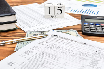 Pay tax concept. Office desk with tax forms, documents with financial, money and cubes with date of 15 april.