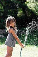 Young girl spraying water on herself with hose in hot summer days