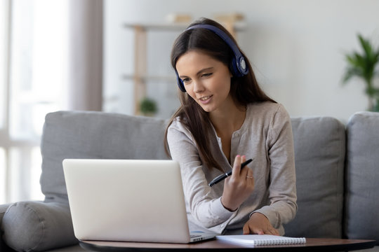 Happy young woman in headphones speaking looking at laptop making notes, girl student talking by video conference call, female teacher trainer tutoring by webcam, online training, e-coaching concept