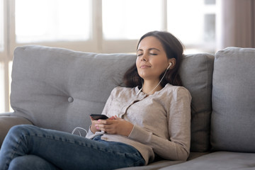 Relaxed teen girl wearing earphones listening to mobile music playing via smartphone app, calm...