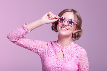 Young girl in love grimaces and funny posing on a pink background with glasses stars pink