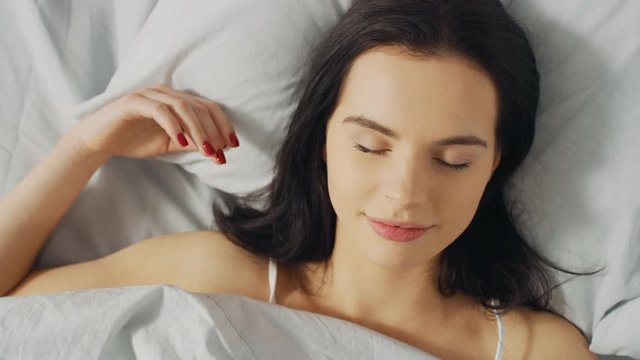 Portrait of Beautiful Young Brunette Charmingly Sleeps in Her Bed in the Early Hours of the Morning. Sweet and Warm View of Girl Sleeping Calmly. Top Down Spinning Camera Shot.