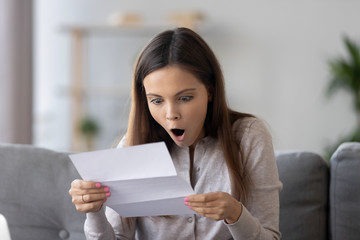 Amazed happy teen girl holding letter reading unbelievable news in paper, surprised shocked woman...