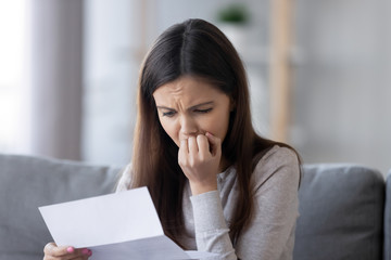 Upset stressed teen girl feeling worried reading bad news in paper mail letter concerned about...
