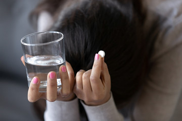 Sad depressed woman or teen in depression holding pill and glass of water desperate troubled with...