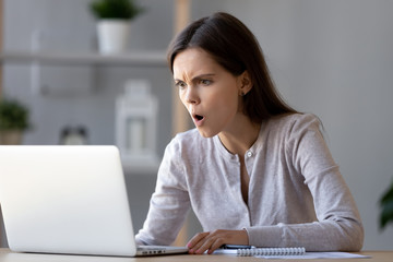 Shocked stressed woman looking at laptop angry reading negative surprise in online news, astonished...
