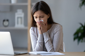 Allergic ill female worker blowing running nose got flu caught cold sneezing in tissue at...