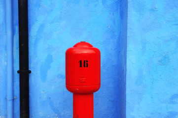 Red fire hydrant on a blue wall background in Burano