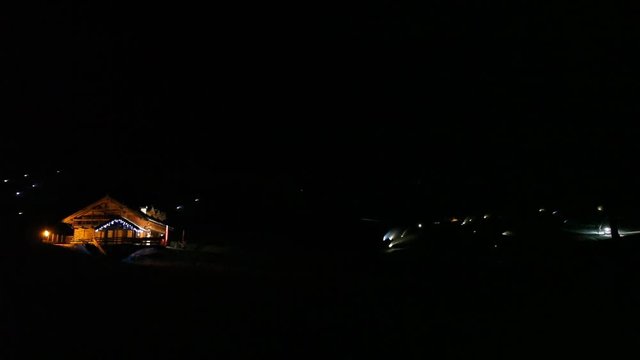 Illuminated chalet in the night with lights of snow cannons on the background