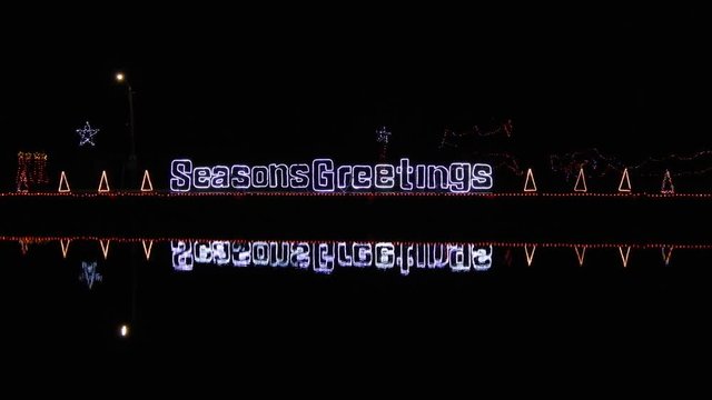 4K Seasons Greeting Sign On Water With 3 Neon Christmas Trees On Either Side