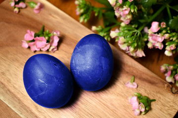 Obraz na płótnie Canvas Blue Easter eggs on a wooden table with pink flowers and petals. Easter holiday concept. 