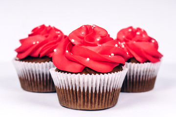 Three delicious cupcakes with vibrant red icing on white background. Close-up.