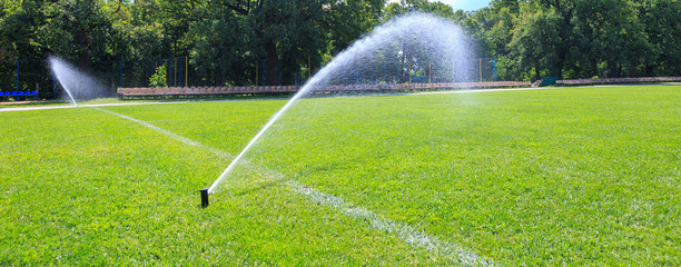 Automatic lawn grass watering system at the stadium. A football, soccer field in a small provincial town. Underground sprinklers spray jets water.