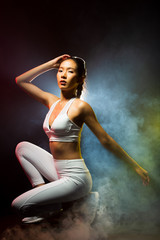 Obraz premium Asian Tan Skin Fitness women exercise wear white gear suit in Fog Smoke Dark background environment, studio lighting yellow back light copy space, concept ready start to run sunglasses
