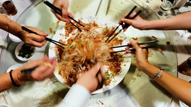 People tossing yee sang or yusheng during Chinese New Year dinner as symbol of good luck
