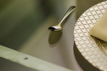 close up of a chrome spoon with a silver plate on one side on a transparent glass table