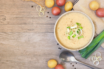 Homemade potato and leek soup. Top view table scene on a light brown wood background with copy...
