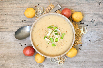 Homemade potato and leek soup. Above view table scene on a light brown wood background.
