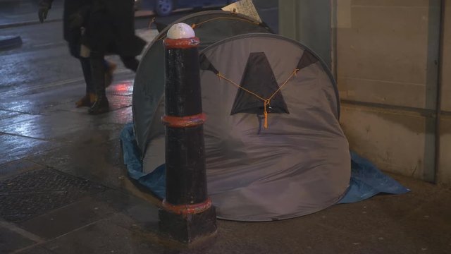 A homeless person in a tent in a city on a snowy night.