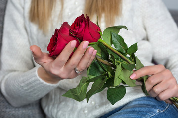 Young woman holding beautiful red rose in hands and sitting in bed at home. Woman day and Valentines day concept. Close up, selective focus