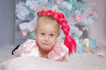 Fototapeta premium Portrait of cute european little blonde princess girl with crown in beautiful dress in decorated studio in christmas location with toys and christmas tree