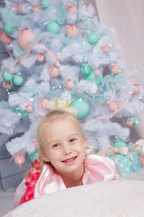 Obraz na płótnie Canvas Portrait of cute european little blonde princess girl with crown in beautiful dress in decorated studio in christmas location with toys and christmas tree