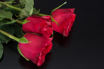 Three red roses flowers on black desk background and space for text or design. Love and romantic concept background. Close up, selective focus
