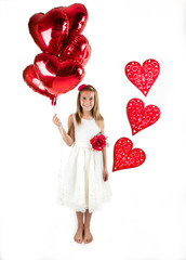 Pretty little girl with white dress celebrating Saint Valentine's Day and holding red shiny balloons in shape of heart on the bright white background