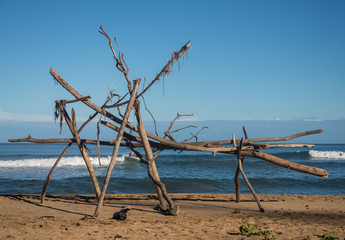 Driftwood structure on Hanalei beach with a surfer visible behind wood