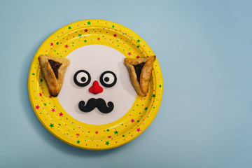 Funny eyes with nose, moustache and Hamantaschen cookies on plate.