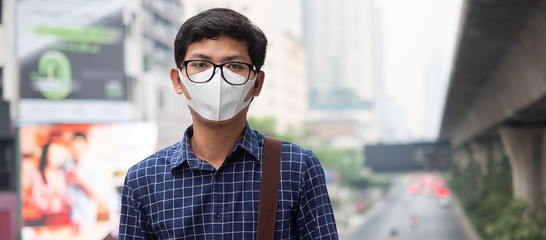 young Asian man wearing N95 respiratory mask protect and filter pm2.5 (particulate matter) against...