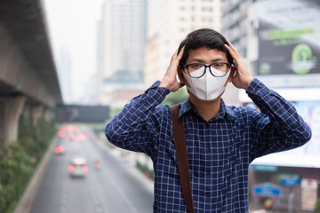 Obraz premium young Asian man wearing N95 respiratory mask protect and filter pm2.5 (particulate matter) against traffic and dust city. healthcare and air pollution concept