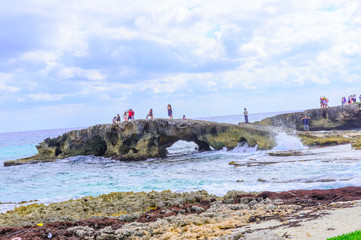 Fototapeta na wymiar People doing photography with dslr cameras,iPhone and selfie sticks on a rock arch on a beach in Cozumel Mexico
