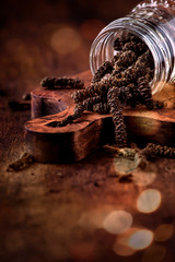 Fragrant long pepper spilling out of glass jar, vintage kitchen table background, selective focus