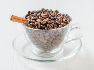 Cinnamon stick in roasted coffee beans in a glass bowl on a white wooden table.