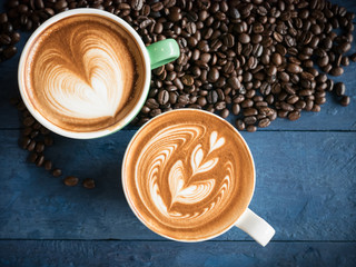 Hot coffee in a cup with foam milk beautiful latte art and coffee beans on blue wooden table background. Cappuccino or latte with froth foam, drinks concept.