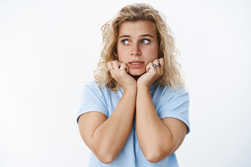 Fototapeta premium Yikes I am in trouble. Portrait of silly and attractive young 25 girl with blue eyes and tan squeez teeth looking scared left and holding hands on jawline concerned and anxious over bad situation