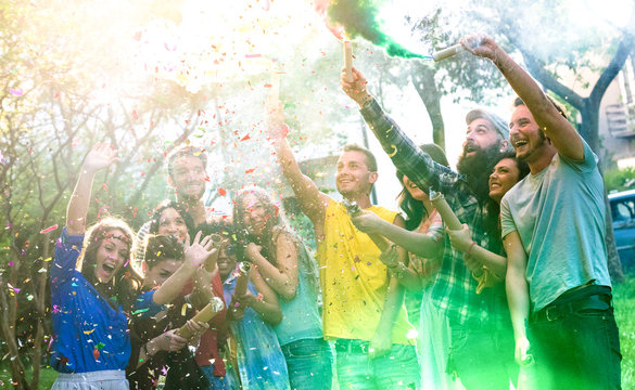 Happy millennial friends having fun at garden party with multicolored smoke bombs outside - Young millenial students celebrating spring break fest together on genuine youth concept - Focus on confetti