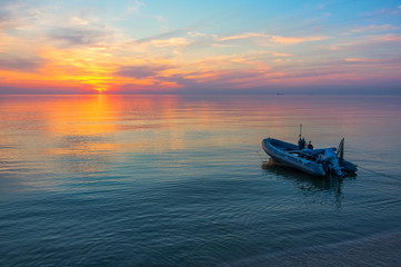 Naklejka na ściany i meble Fishing boat in the calm sea on a background of a beautiful sunset with ships on the horizon