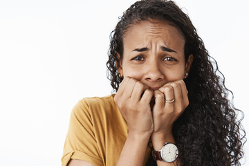 Fototapeta na wymiar Close-up shot of freaked-out upset crying african american woman being scared and terrified trembling from fear biting fingernails and frowning panicking cannot calm down over gray background