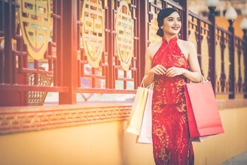 Chinese girl wearing Cheongsam and smile happily. Holding her shopping bags after a lot of shopping malls in Chinatown and was walking on the sidewalk. Amid the atmosphere of the evening sun.