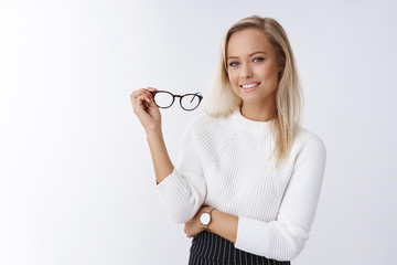 Woman trying new glasses in store picking right frame fits style posing over white background confident and satisfied smiling pleased holding eyewear in arm feeling self-assured and successful - obrazy, fototapety, plakaty