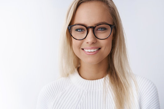 Elegant attractive young businesswoman in glasses smiling delighted, satisfied with new frame of eyewear gazing friendly happily at camera reaching success ready share tips over white wall