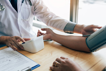 Asian doctor female measuring blood pressure of male patient at clinic office room.